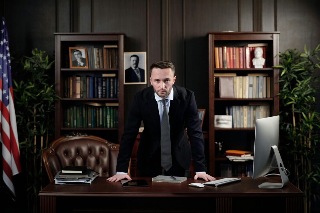 Confident businessman standing at desk with USA flag in office library.